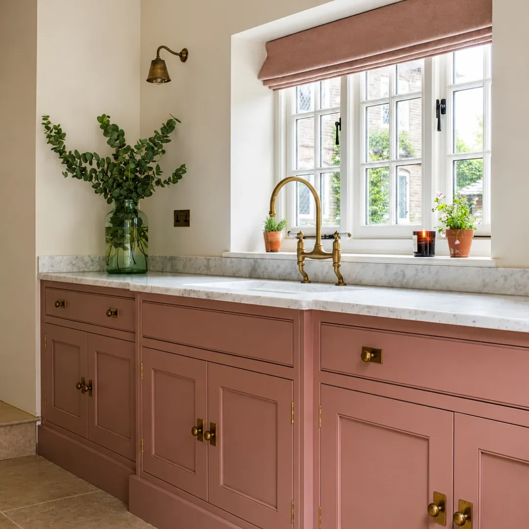 Kitchen tiling with pink cabinets, marble worktop and brass tap by a window