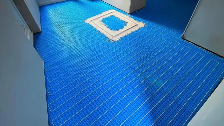 Blue underfloor heating mat and cable layout across a bathroom floor before tiling
