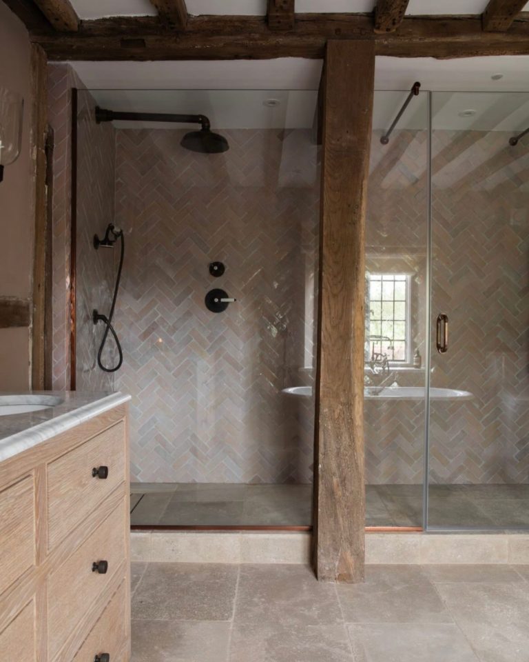 Wet room installation with exposed beams, herringbone shower tiles and glass shower screen