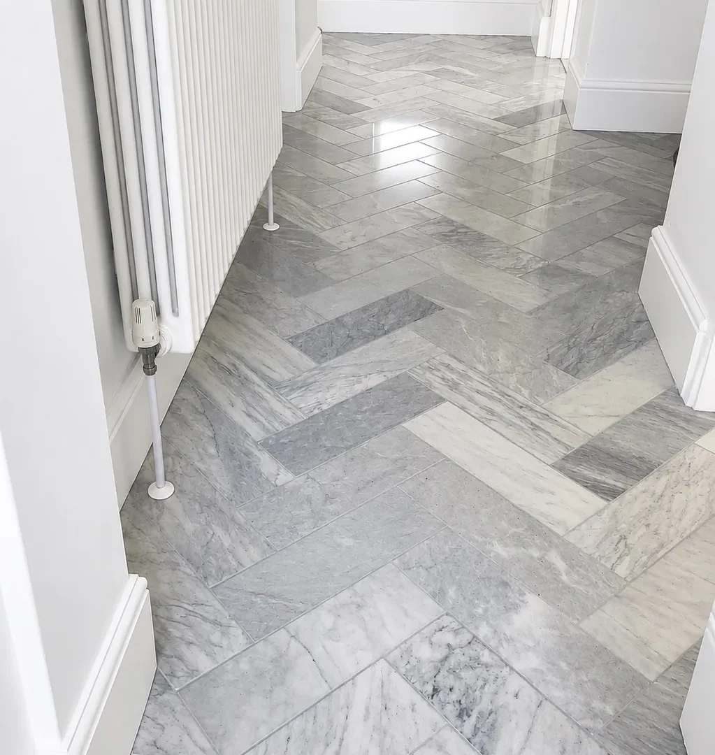 Entrance floor before renovation with grey marble herringbone tiles and white radiator.