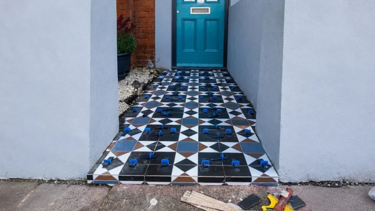 Porcelain front path tiles being set out with blue levelling clips in front of a blue entrance door.