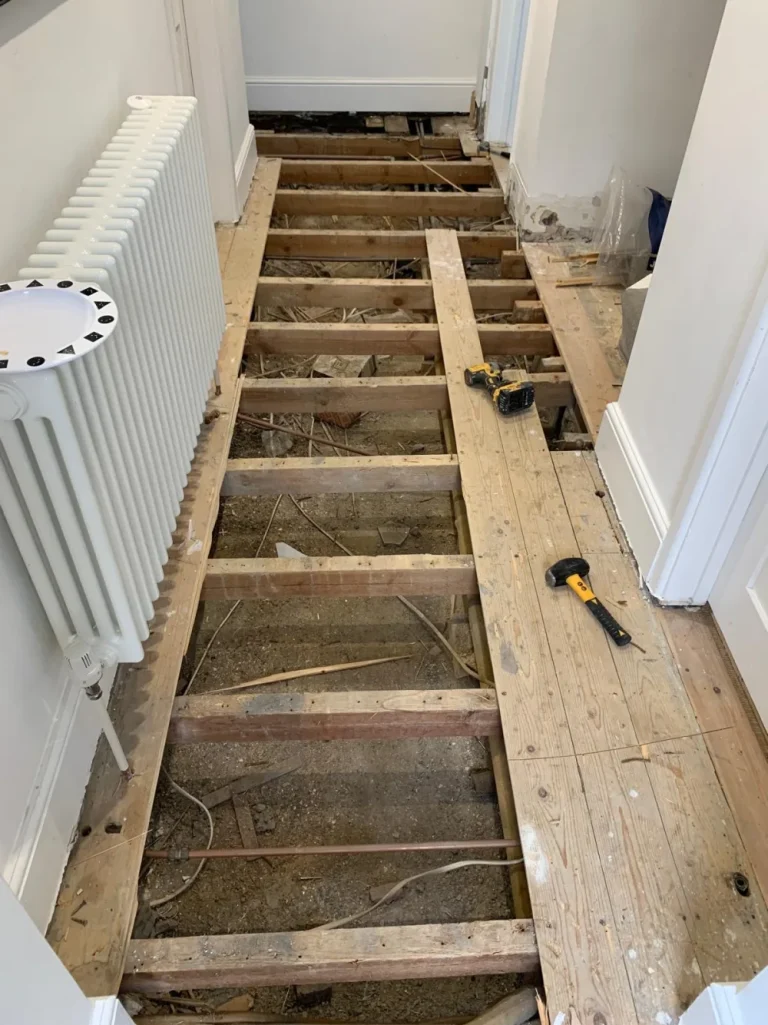 Exposed suspended timber floor joists in a hallway before structural reinforcement and tiling preparation.