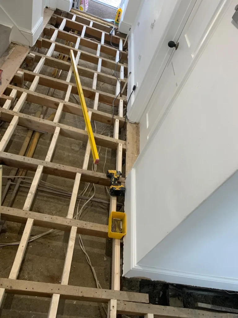 Suspended timber floor reinforcement with new timber noggins and joist strengthening in a London hallway.