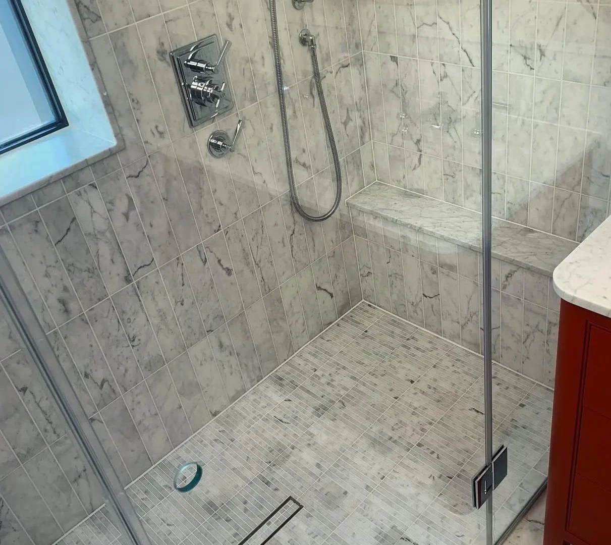 Marble tiled wet room shower with mosaic floor, glass enclosure and built-in shower bench.
